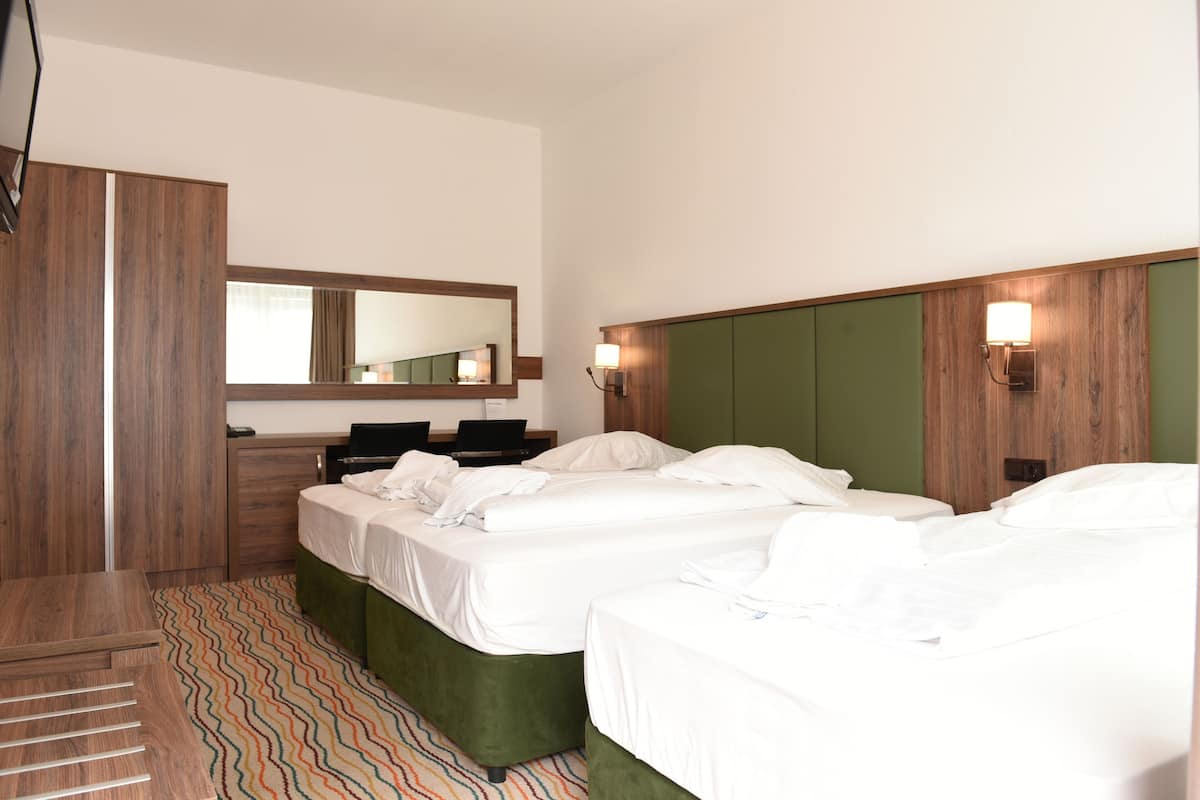 Una habitación de hotel con dos camas, un espejo, un escritorio y un banco tapizado en verde.