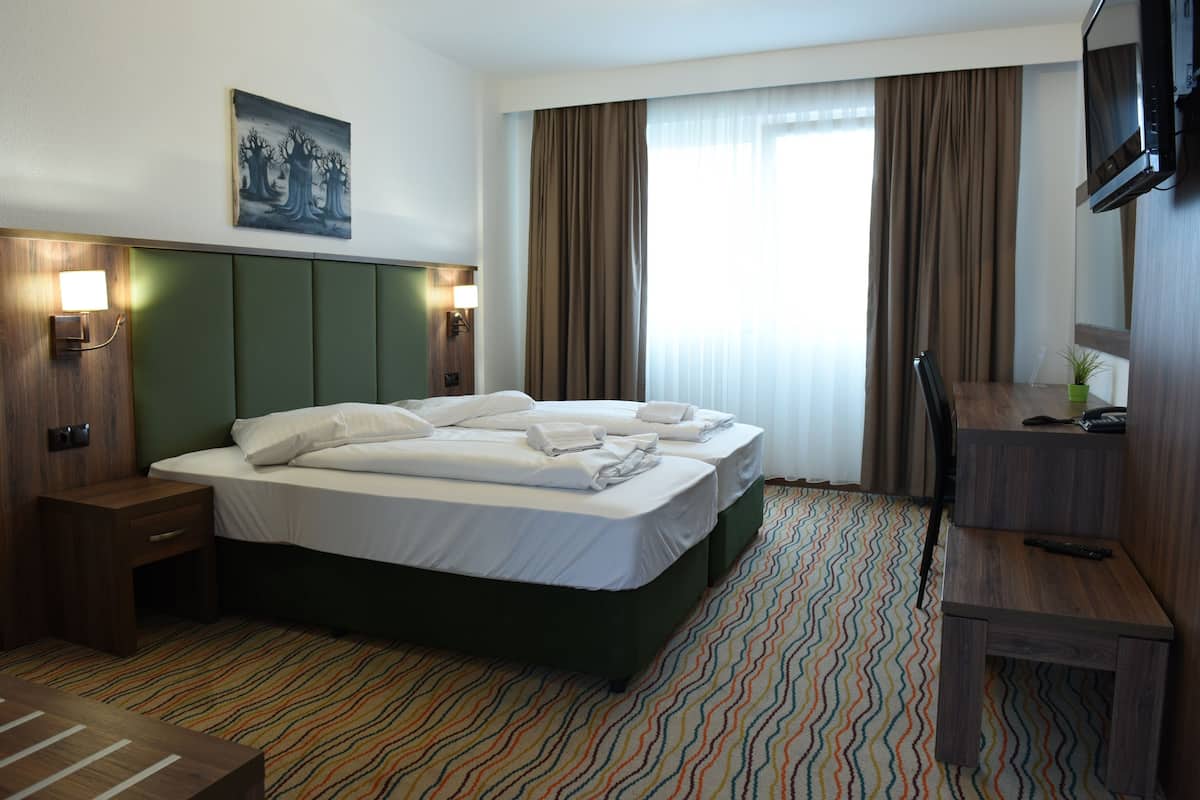 Habitación de hotel con una cama grande, un escritorio, una silla, un televisor y un cuadro en la pared.