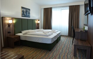 Habitación de hotel con una cama grande, un escritorio, una silla, un televisor y un cuadro en la pared.