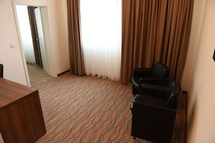 Ein Hotelzimmer mit einem gemusterten Teppich, einem Holztisch, einem schwarzen Sessel und Blick durch ein Fenster mit Vorhängen.