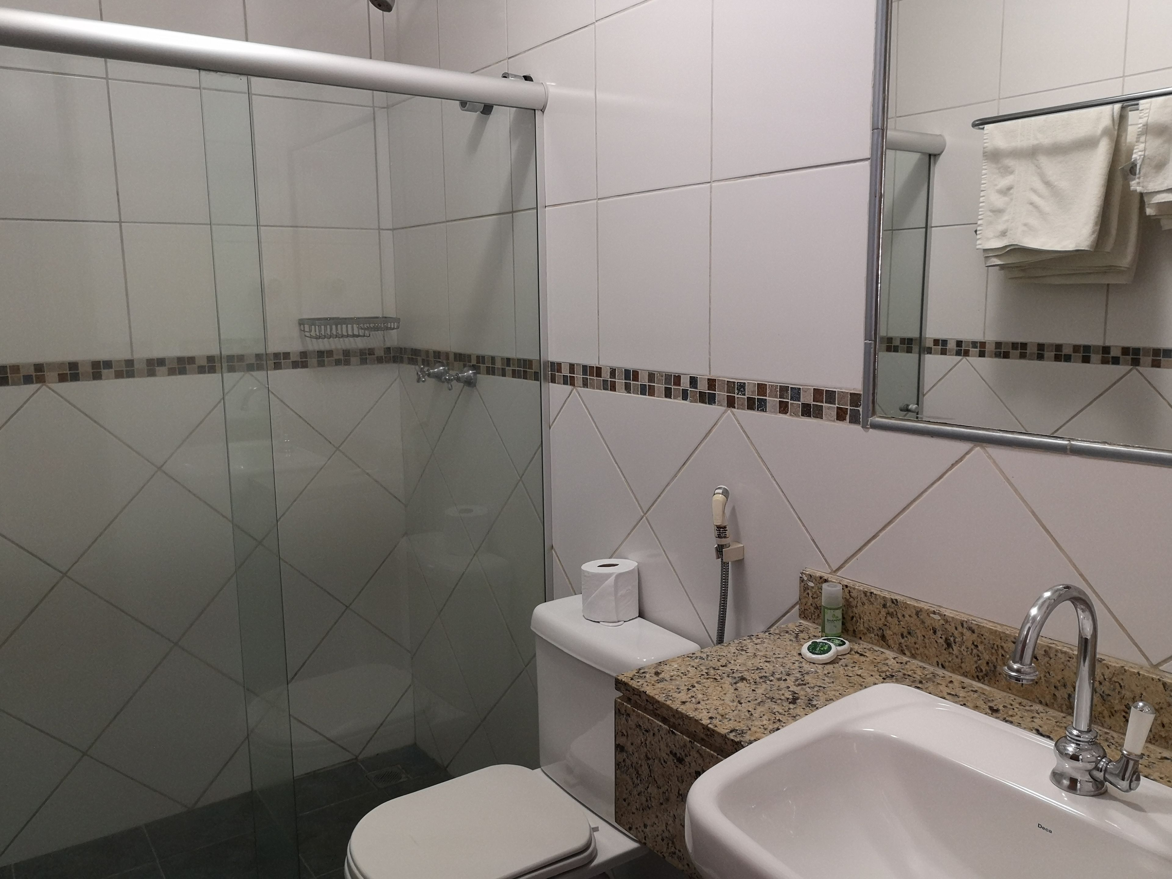 Un baño con ducha de vidrio, inodoro, lavamanos con encimera de granito y espejo sobre el lavamanos.