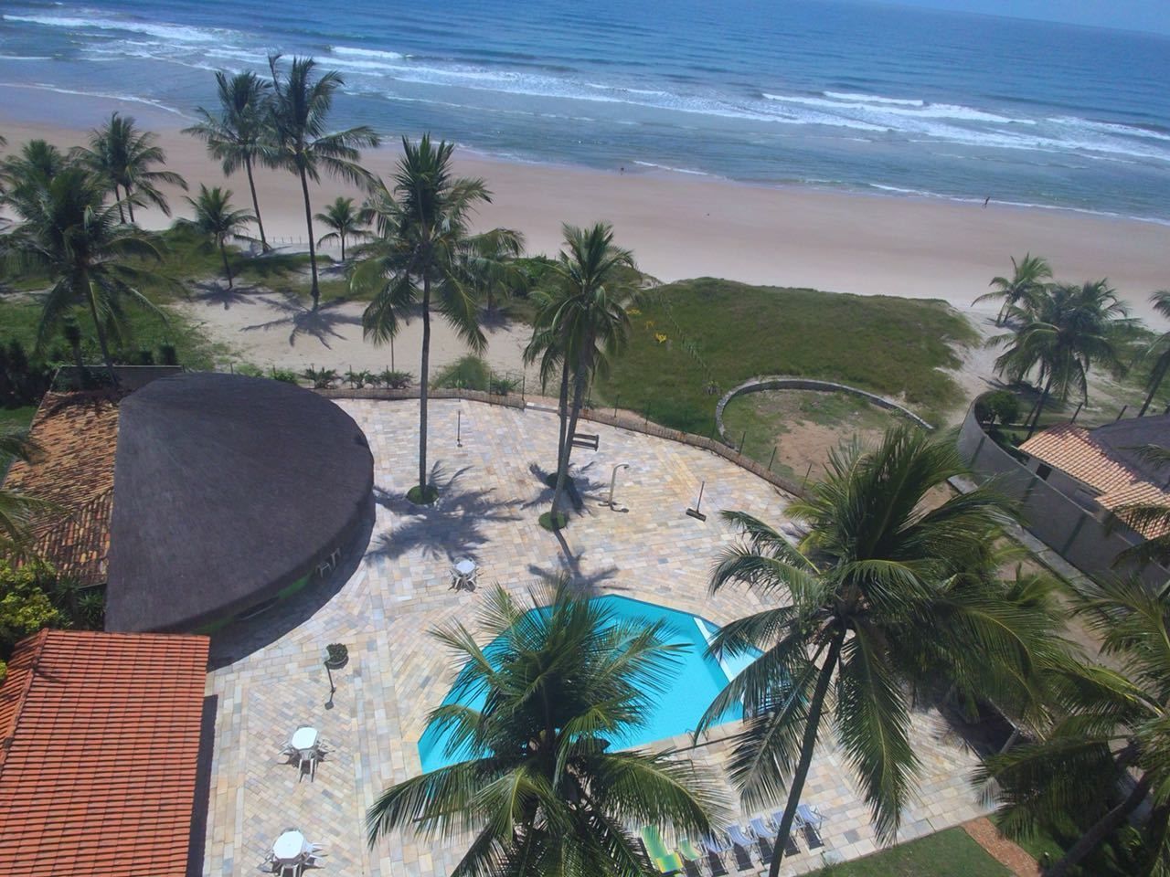 A pool area with a view of the beach and ocean, surrounded by palm trees and a tiled deck.