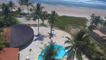 A pool area with a view of the beach and ocean, surrounded by palm trees and a tiled deck.