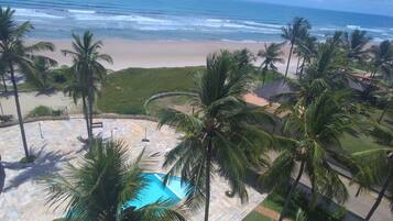 Área de piscina com palmeiras, praia e vista para o oceano.