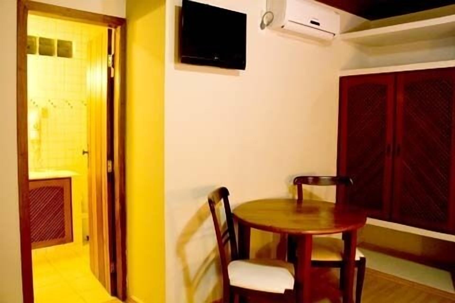 Una habitación con una mesa y sillas de madera, un televisor montado en la pared y un armario rojo.