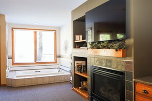 A living room with a fireplace, a large window with blinds, and a built-in shelf with decorative items.