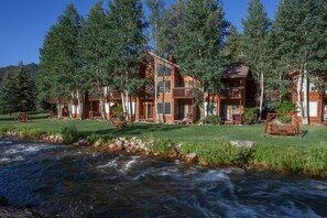 A lodge with multiple wooden cabins, a river in the foreground, and a forested backdrop. - Aspen Winds on Fall River (Estes Park)