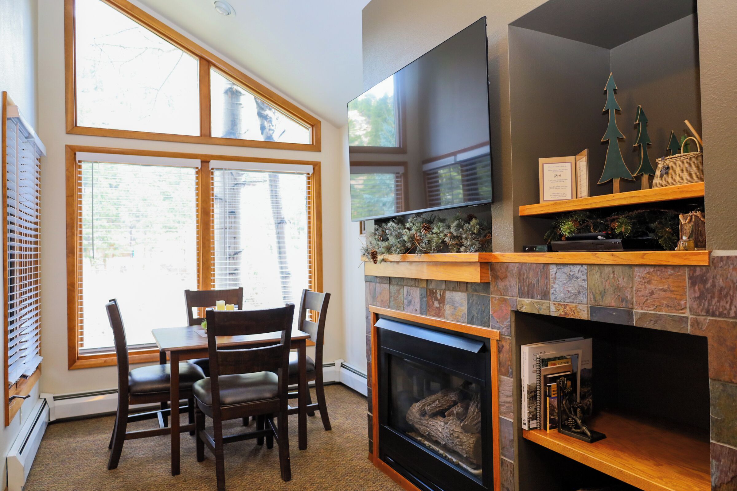 A cozy living room with a fireplace, a dining area with a table and chairs, and a large window with blinds.