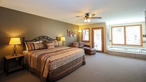 A bedroom with a large bed, a nightstand, a reading lamp, a ceiling fan, a window with blinds, and a small window seat. - Aspen Winds on Fall River (Estes Park)