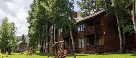 A wooden cabin with a balcony, surrounded by trees and a grassy yard.