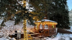 A gazebo with string lights, a barbecue grill, and a snow-covered deck. - Aspen Winds on Fall River (Estes Park)