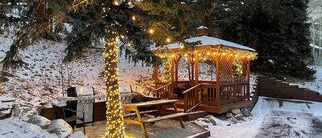 A gazebo with string lights, a barbecue grill, and a snow-covered deck.