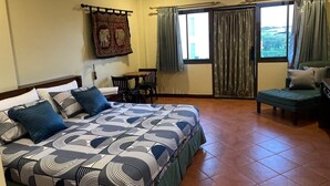 Une chambre à coucher comprenant un lit, un bureau, une chaise et un canapé. On y trouve une fenêtre avec des rideaux, un appareil de climatisation et un tableau accroché au mur.