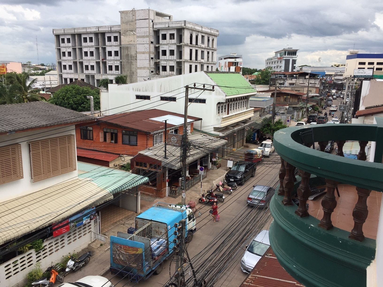Vista de la calle con edificios, vehículos y una estructura verde con balcón.
