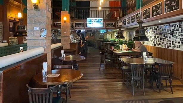 L’intérieur d’un restaurant avec des tables en bois, des piliers en pierre et un espace bar.