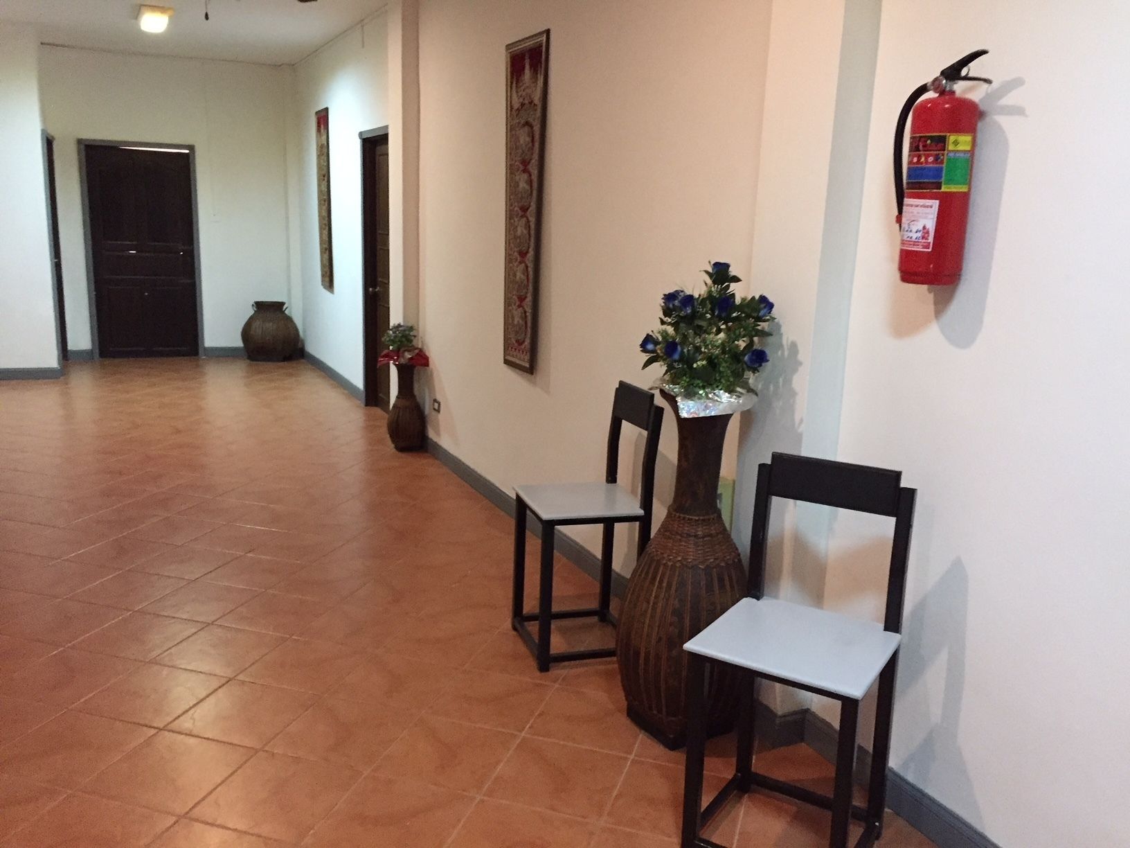 Un pasillo con un extintor en la pared, un jarrón con flores y dos sillas.