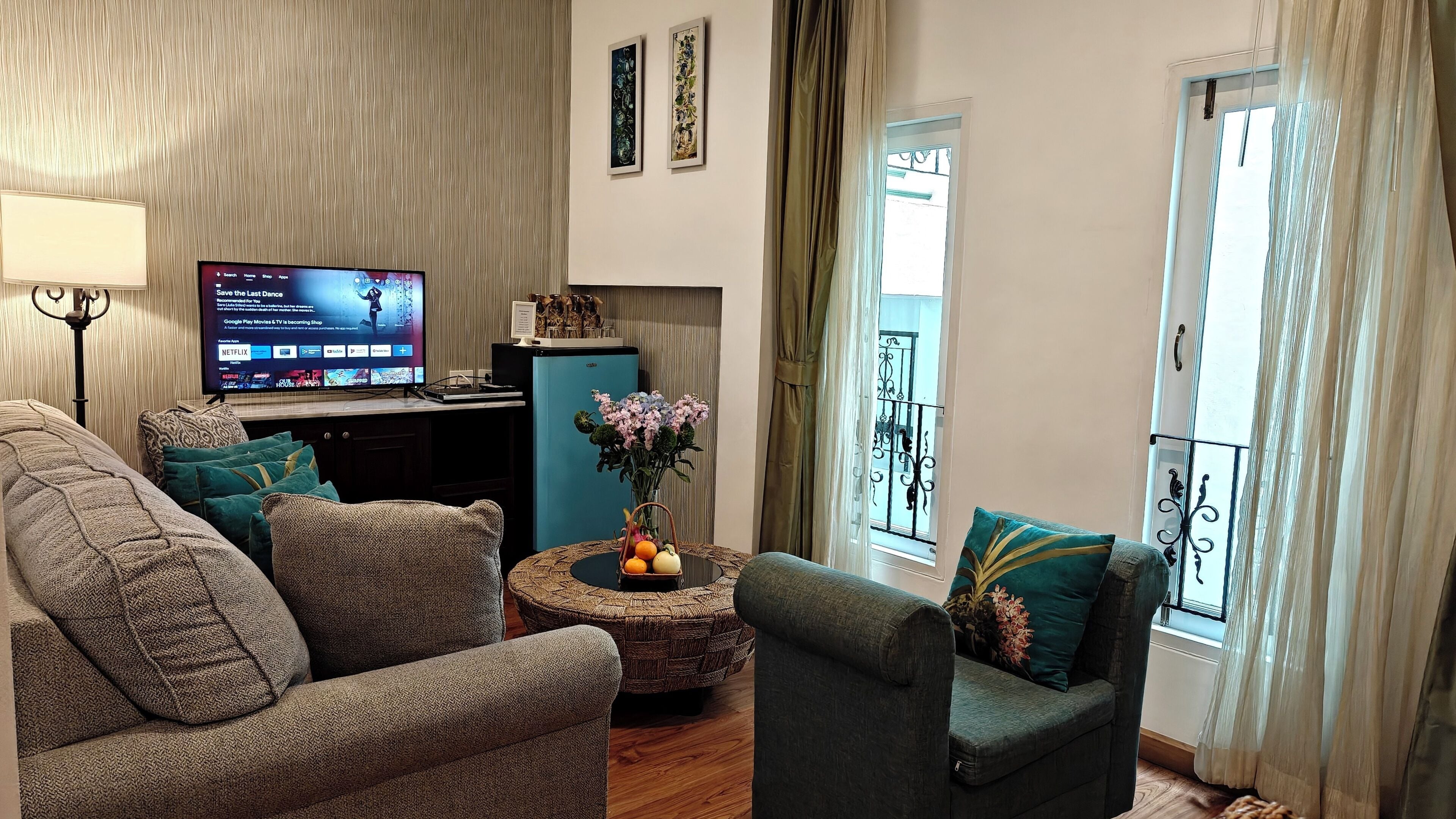 A living room with a TV, sofa, armchair, and a small table with a vase and oranges.