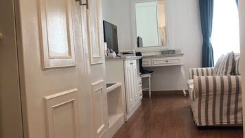 Une chambre avec un plancher en bois, un lit, une commode, un bureau avec un miroir et une fenêtre avec des rideaux.