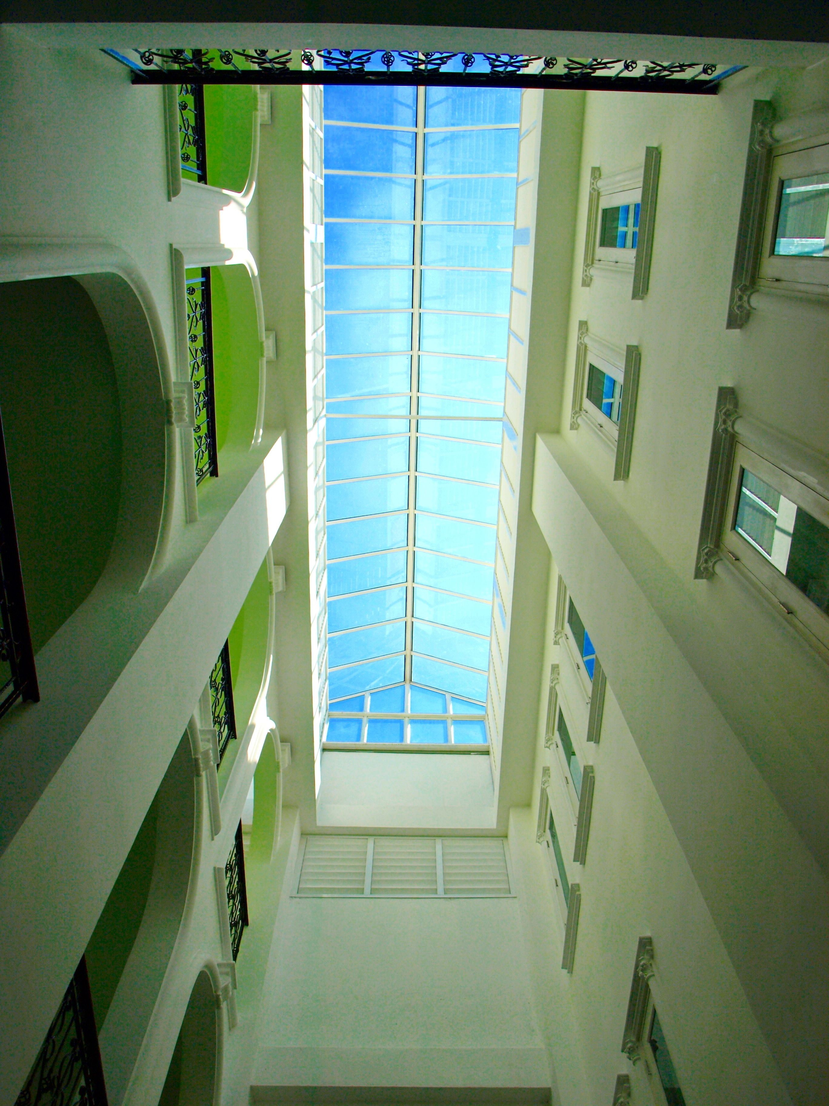 Un atrium à plusieurs niveaux, doté d’une verrière centrale, de murs blancs et de touches de vert.