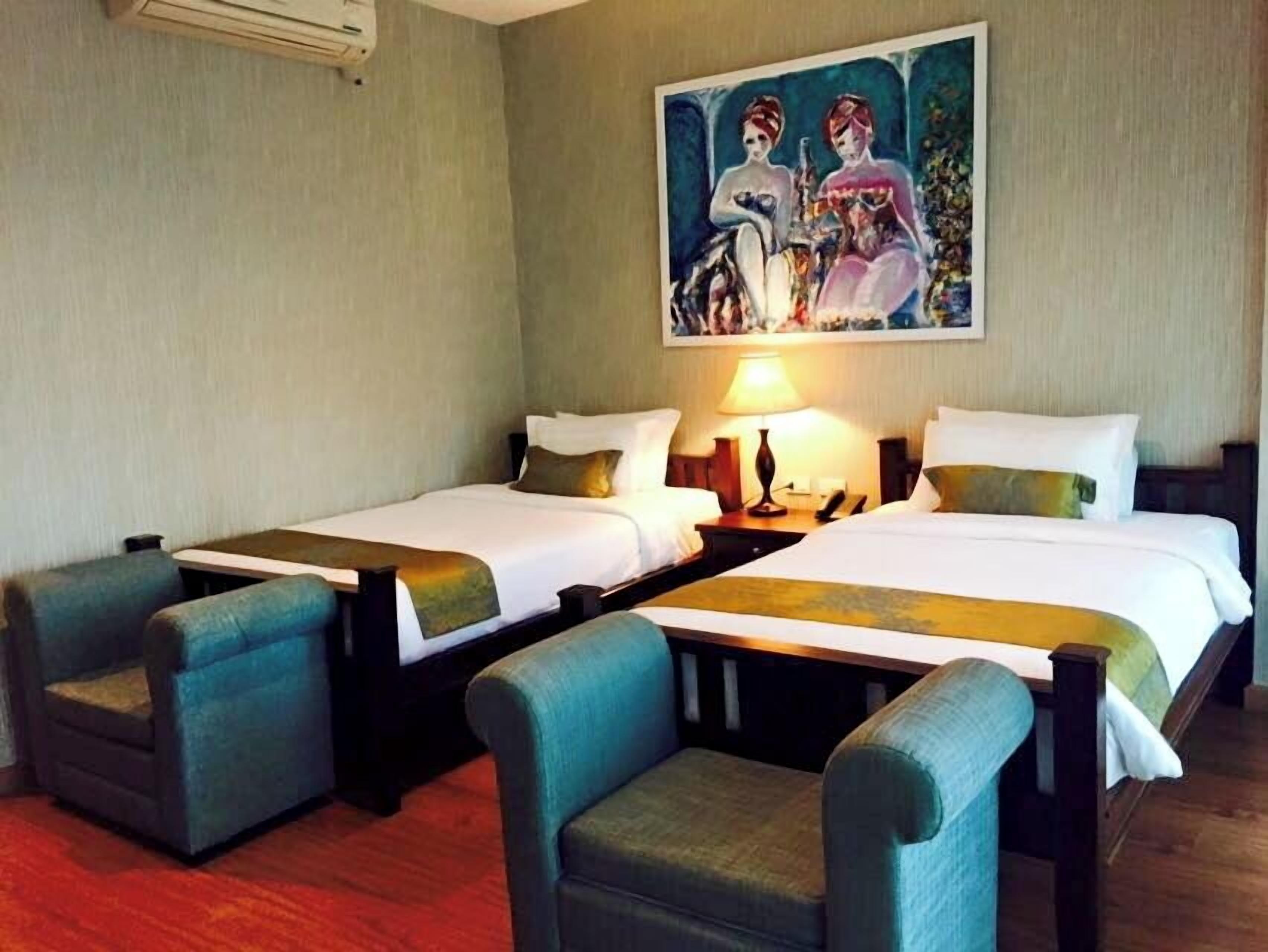 Quarto de hotel com duas camas, um quadro na parede e um abajur entre as camas.