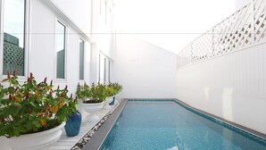 Una piscina con paredes blancas y suelo de baldosas, rodeada de plantas en macetas y una valla blanca.