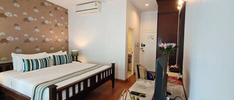 Un dormitorio con cama, lámpara de noche, aire acondicionado y un mueble de televisión con un florero.