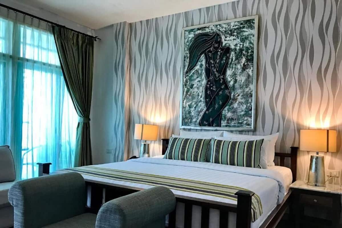 Una habitación de hotel con cama, dos lámparas de noche, una silla y un cuadro abstracto grande en la pared.