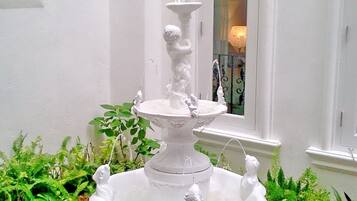 A white, multi-tiered fountain with statues in a garden setting.