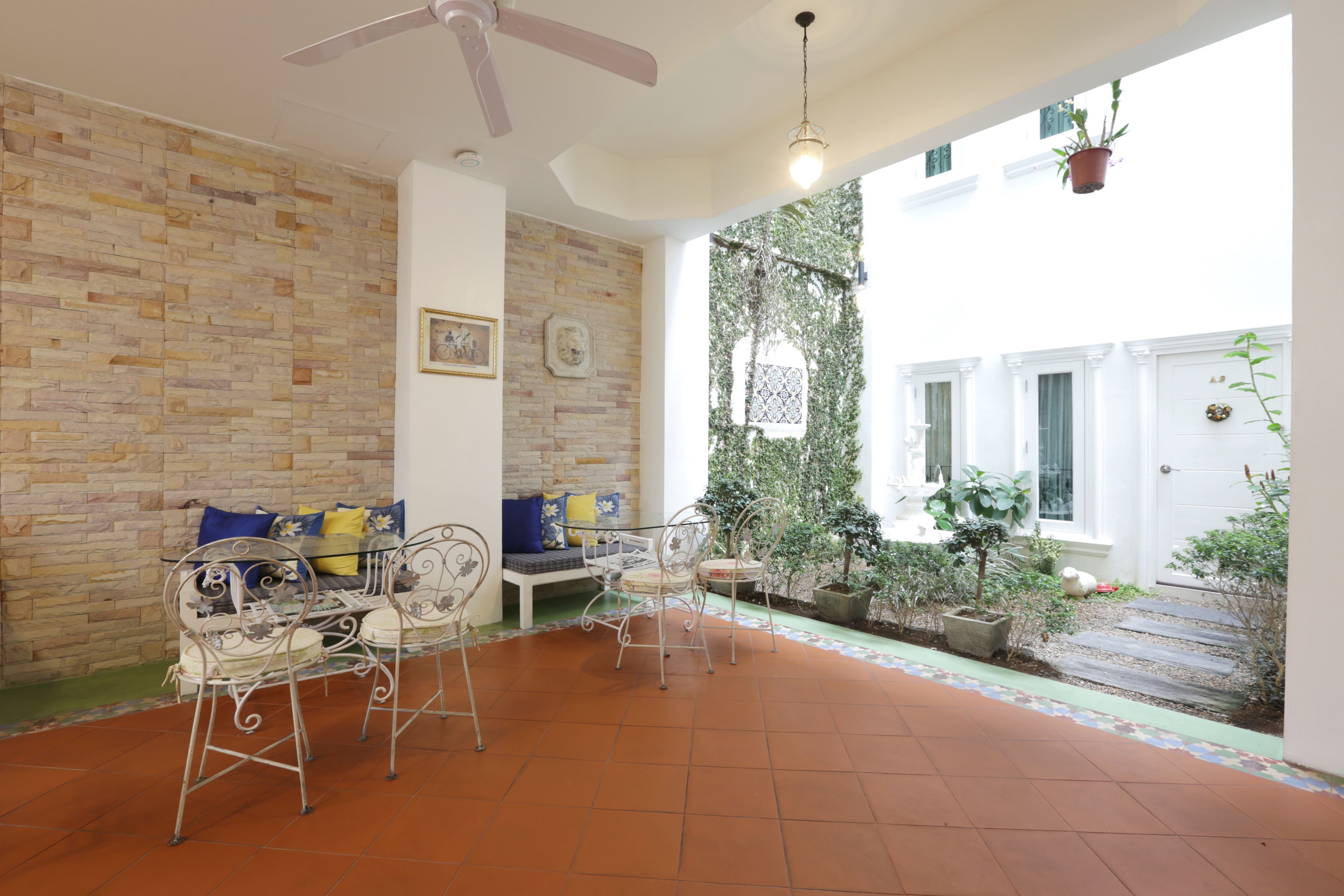 A spacious patio with a brick floor, a ceiling fan, and a seating area with metal chairs and a sofa.