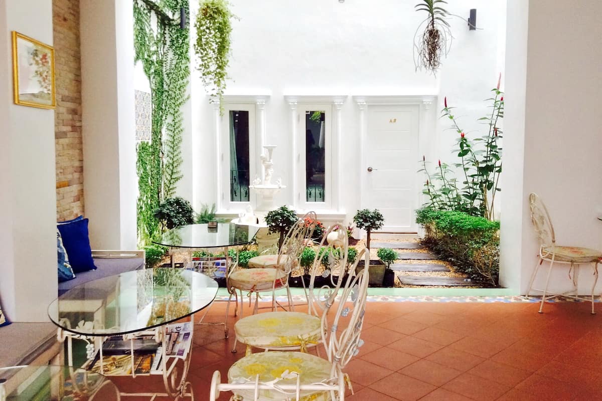 Un amplio salón con una mesa y sillas de vidrio, una puerta blanca y diversas plantas de interior.