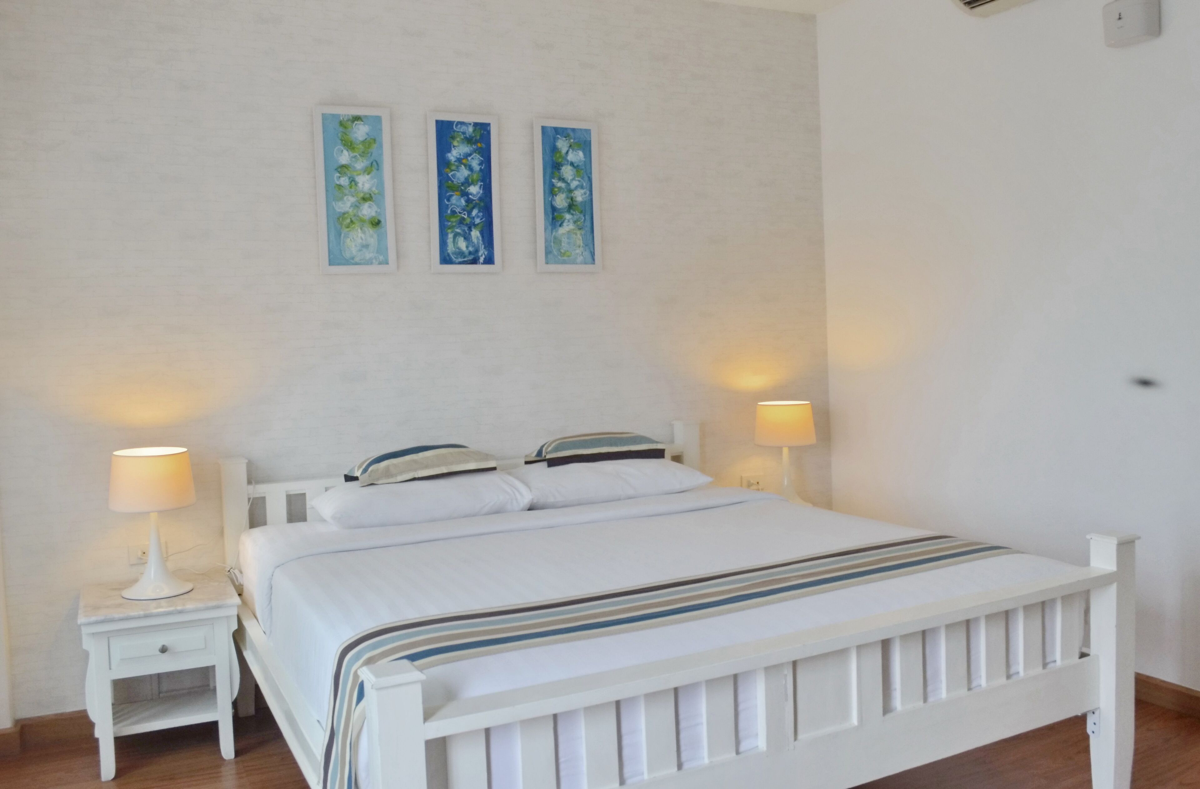 A bedroom with a white bed, two bedside tables, and three wall-mounted paintings.