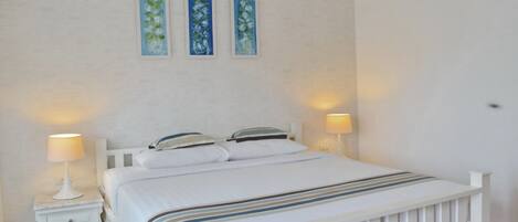 A bedroom with a white bed, two bedside tables, and three wall-mounted paintings.