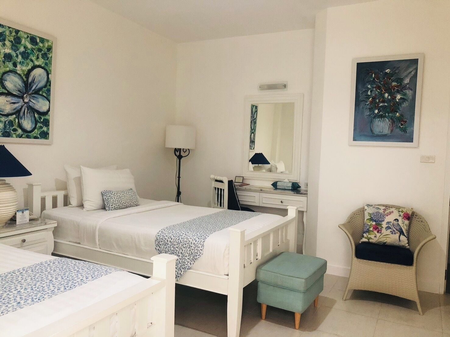 A bedroom with a bed, bedside tables, a lamp, a dresser, a chair, and two paintings.