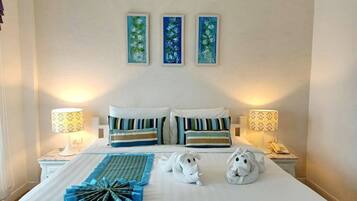 Un lit bien fait, agrémenté d’oreillers à rayures, d’un objet décoratif bleu et de deux serviettes blanches en forme d’animaux. Trois tableaux sont accrochés au mur au-dessus du lit.