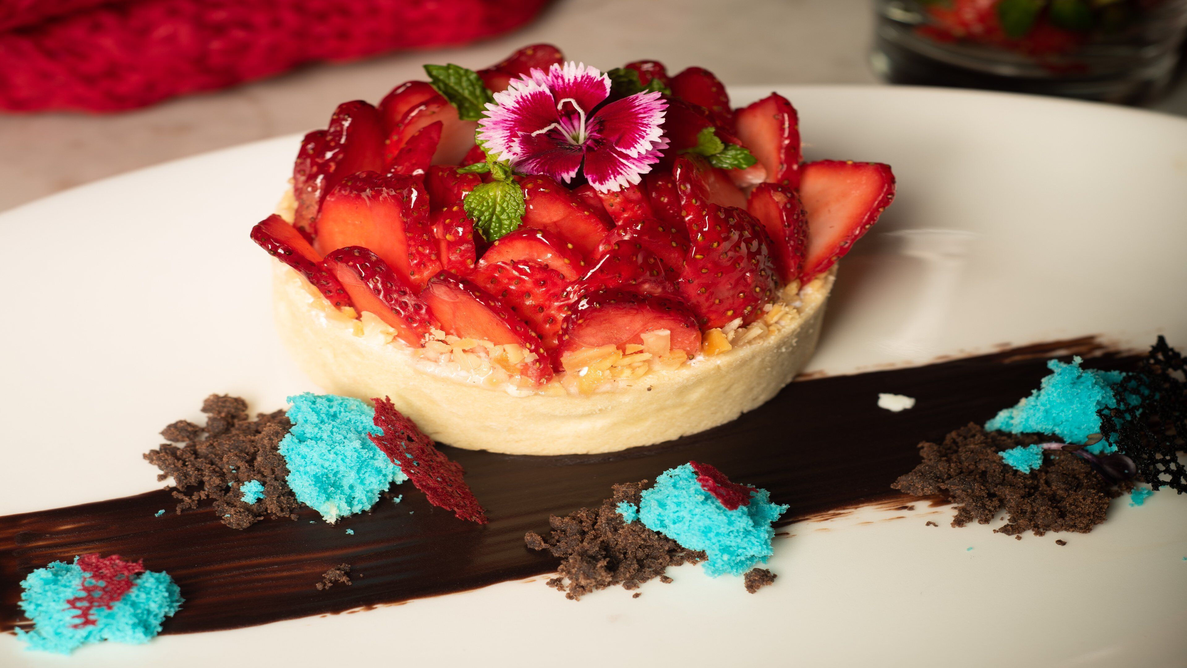 A dessert with strawberries and a flower on top, placed on a white plate with chocolate shavings around it.