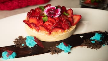 A dessert with strawberries and a flower on top, placed on a white plate with chocolate shavings around it.