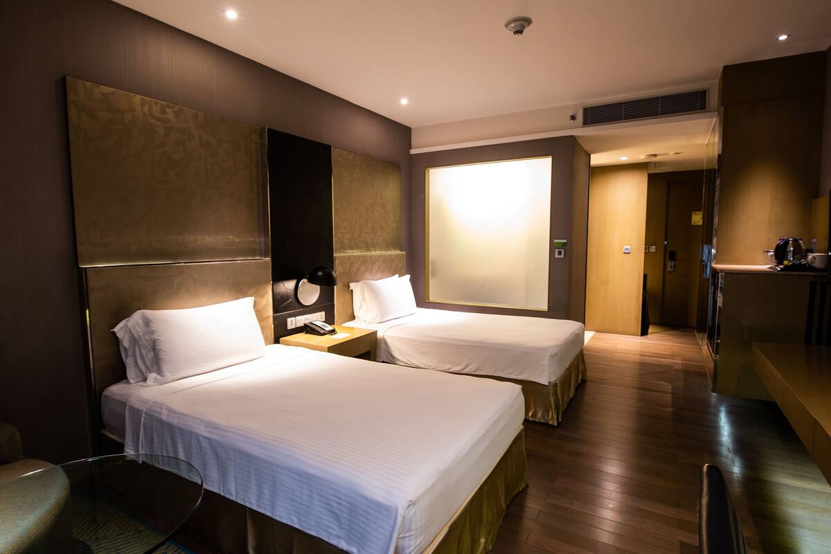 A hotel room with two beds, a desk, a chair, and a large window.