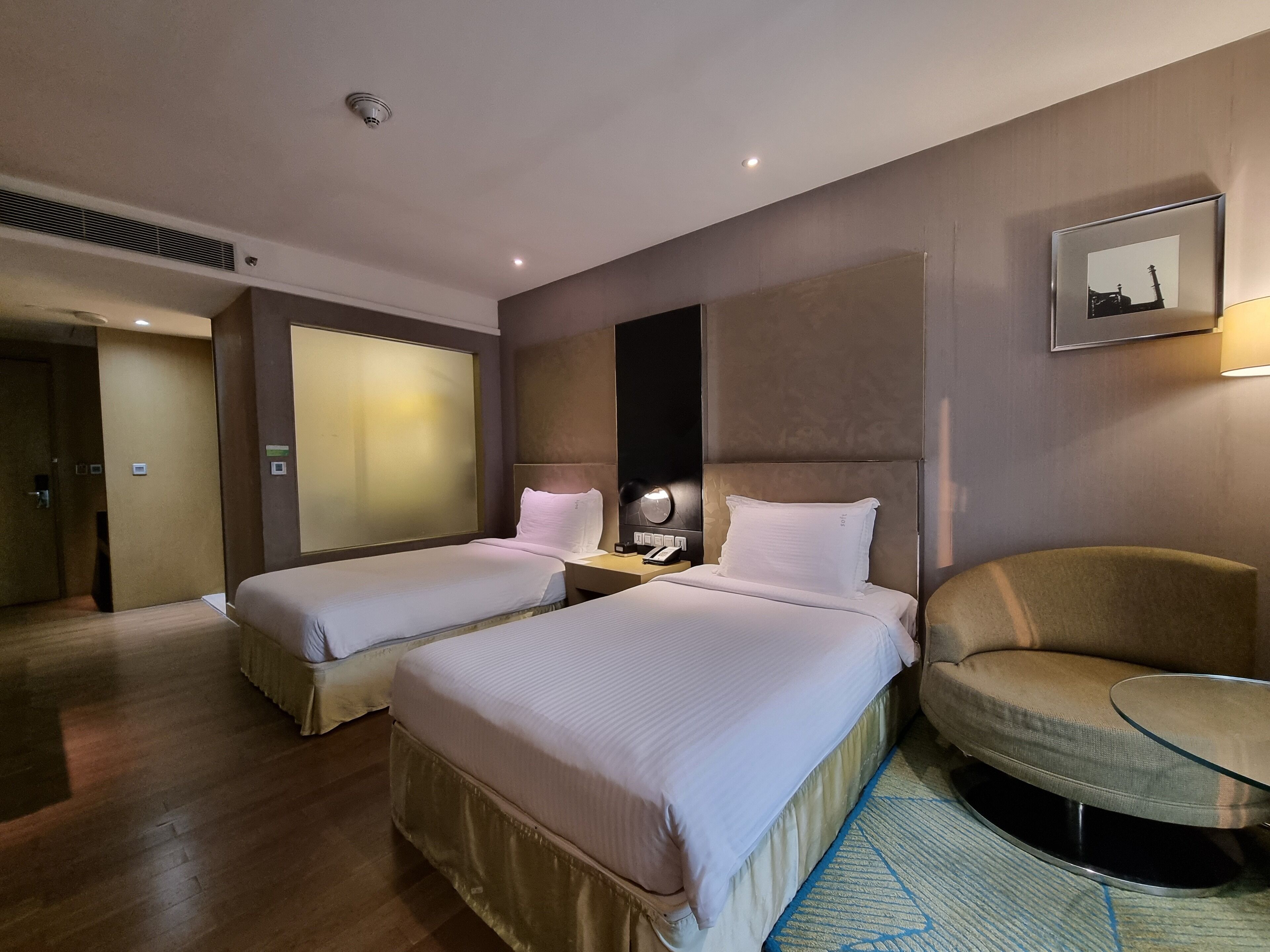 A hotel room with two beds, a sitting area with a chair and a small table, and a wall-mounted picture.