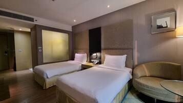 A hotel room with two beds, a sitting area with a chair and a small table, and a wall-mounted picture.
