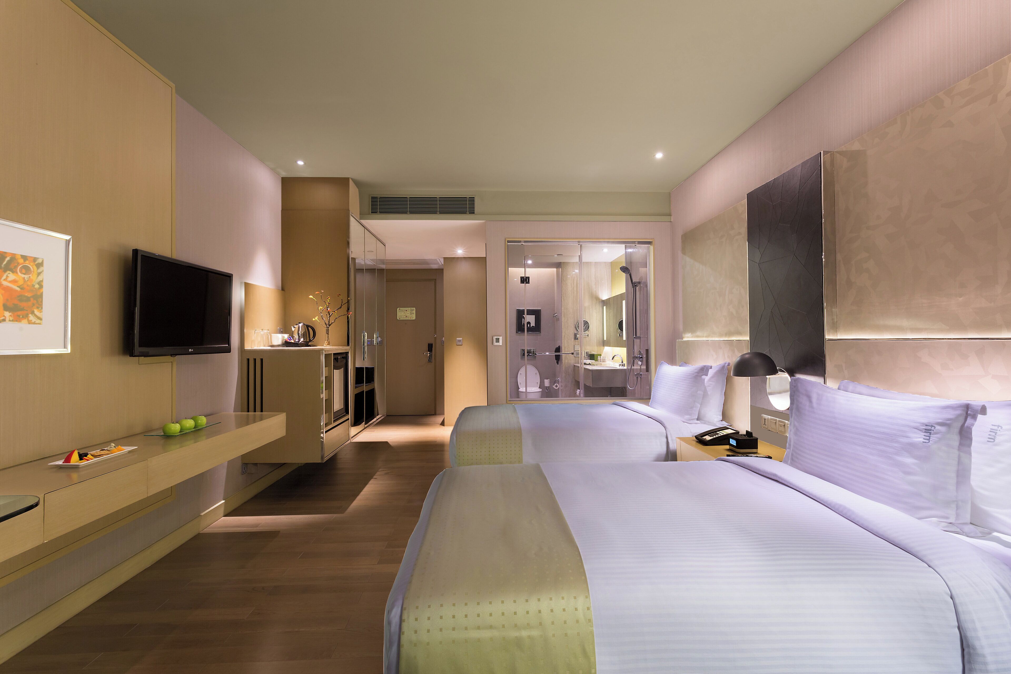 Une chambre d’hôtel moderne avec un grand lit, une table de chevet, un téléviseur à écran plat et une salle de bain visible à travers une porte ouverte.