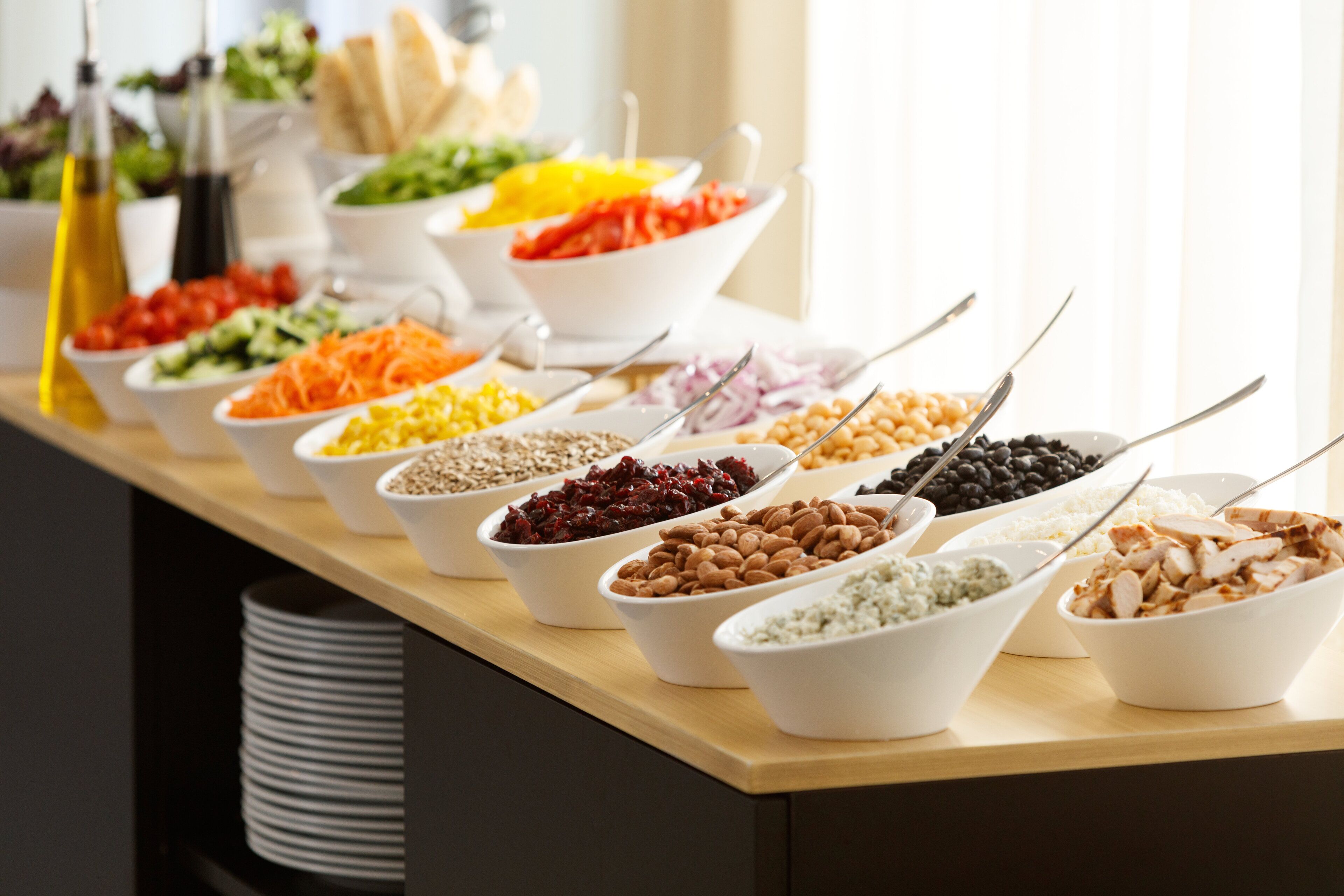 A buffet table with various food items in white bowls, including salads, grains, and legumes.