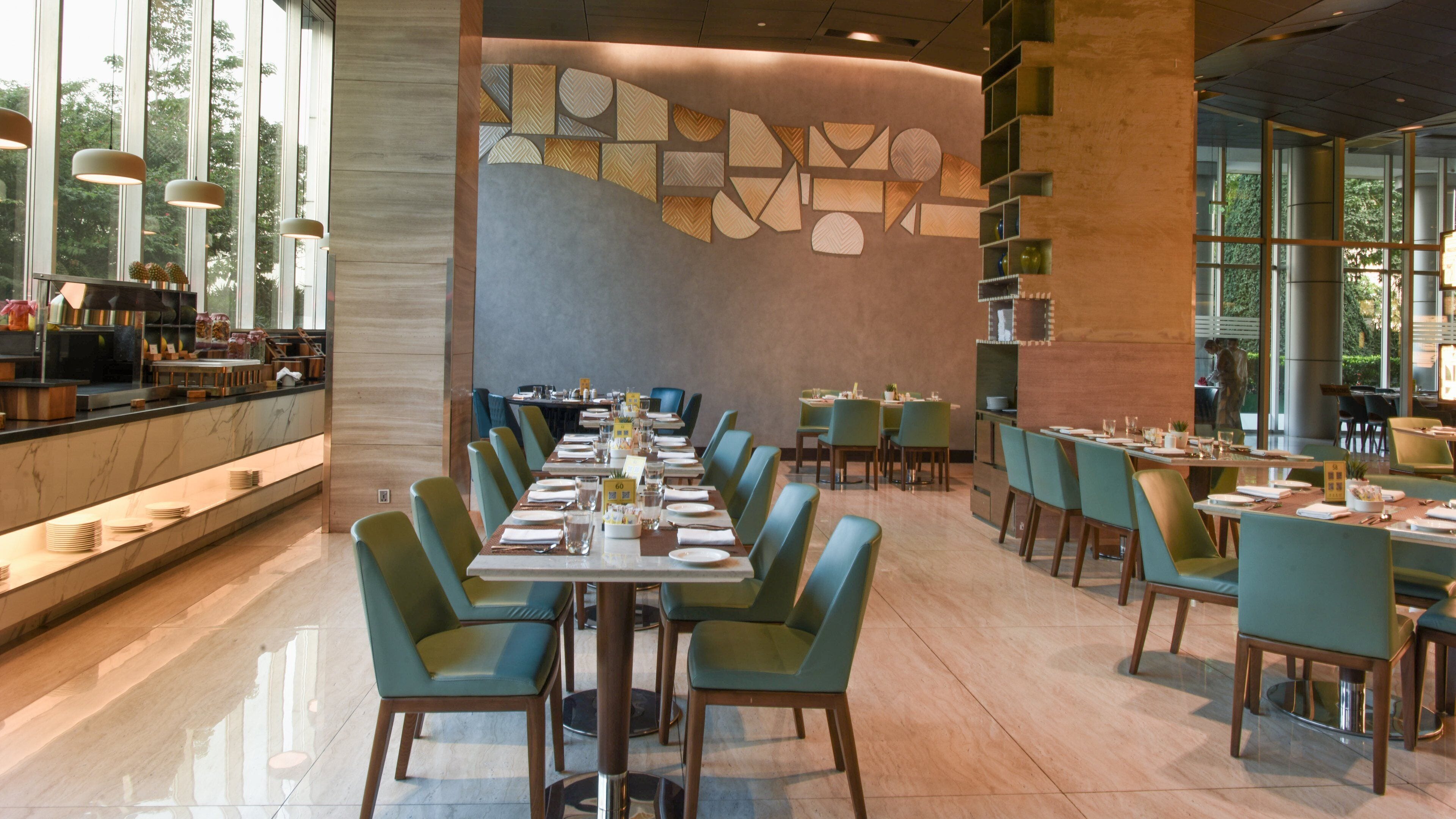 Un restaurant moderne avec une longue table à manger dressée pour le repas, entourée de chaises vertes.
