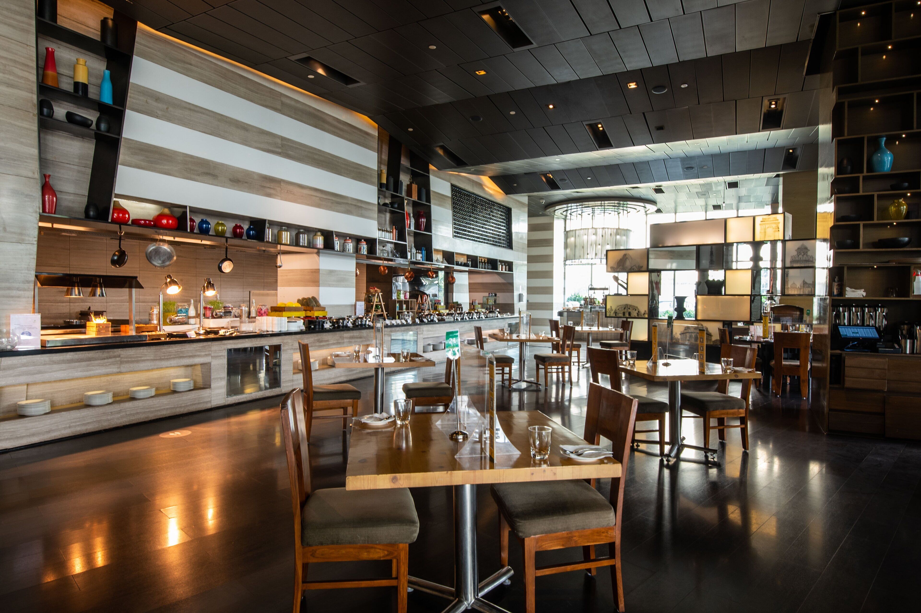 A modern restaurant with a bar area, wooden tables and chairs, and a variety of kitchen utensils and decorations on shelves.