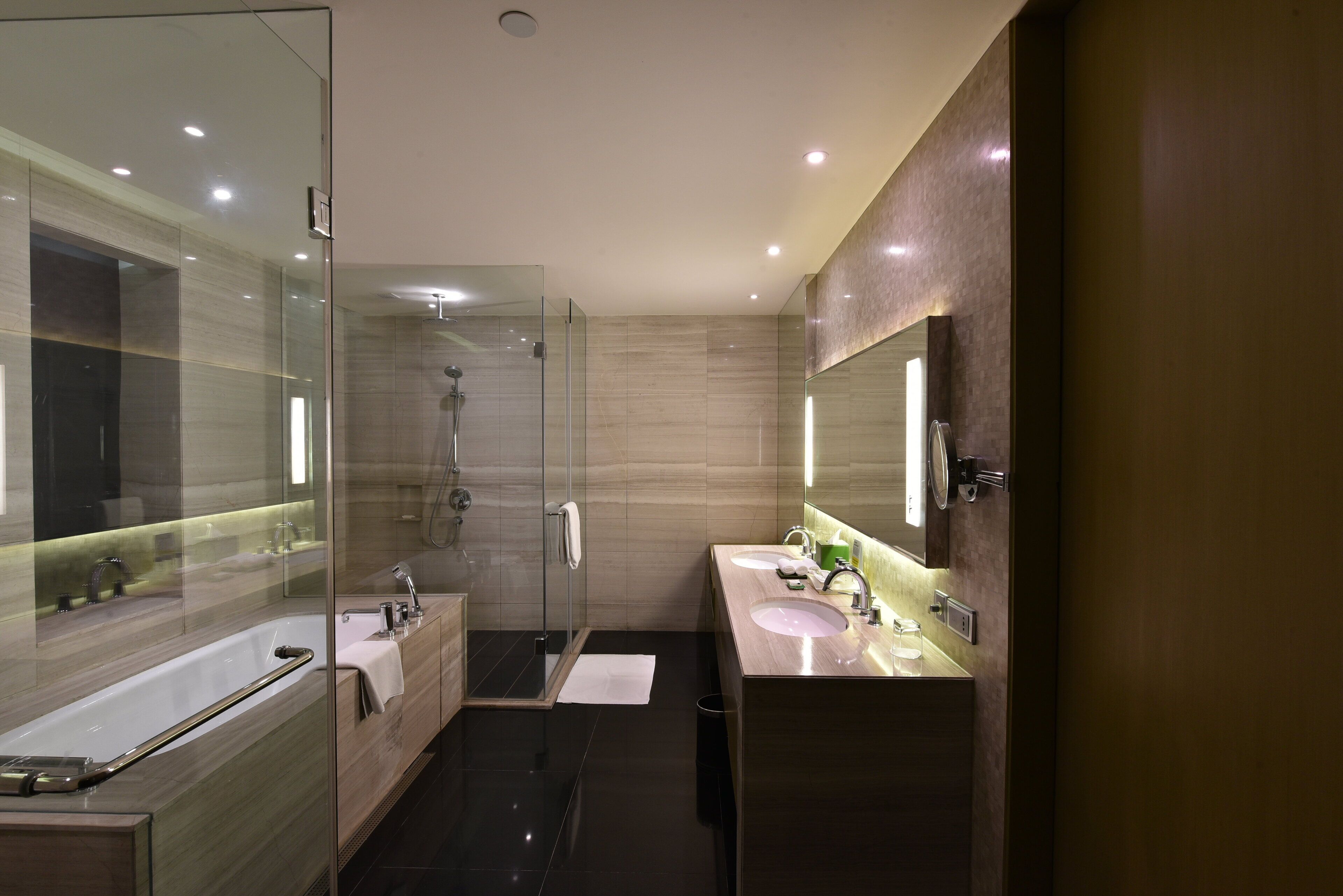 Un baño moderno con cabina de ducha de vidrio, dos lavamanos y un espejo grande.
