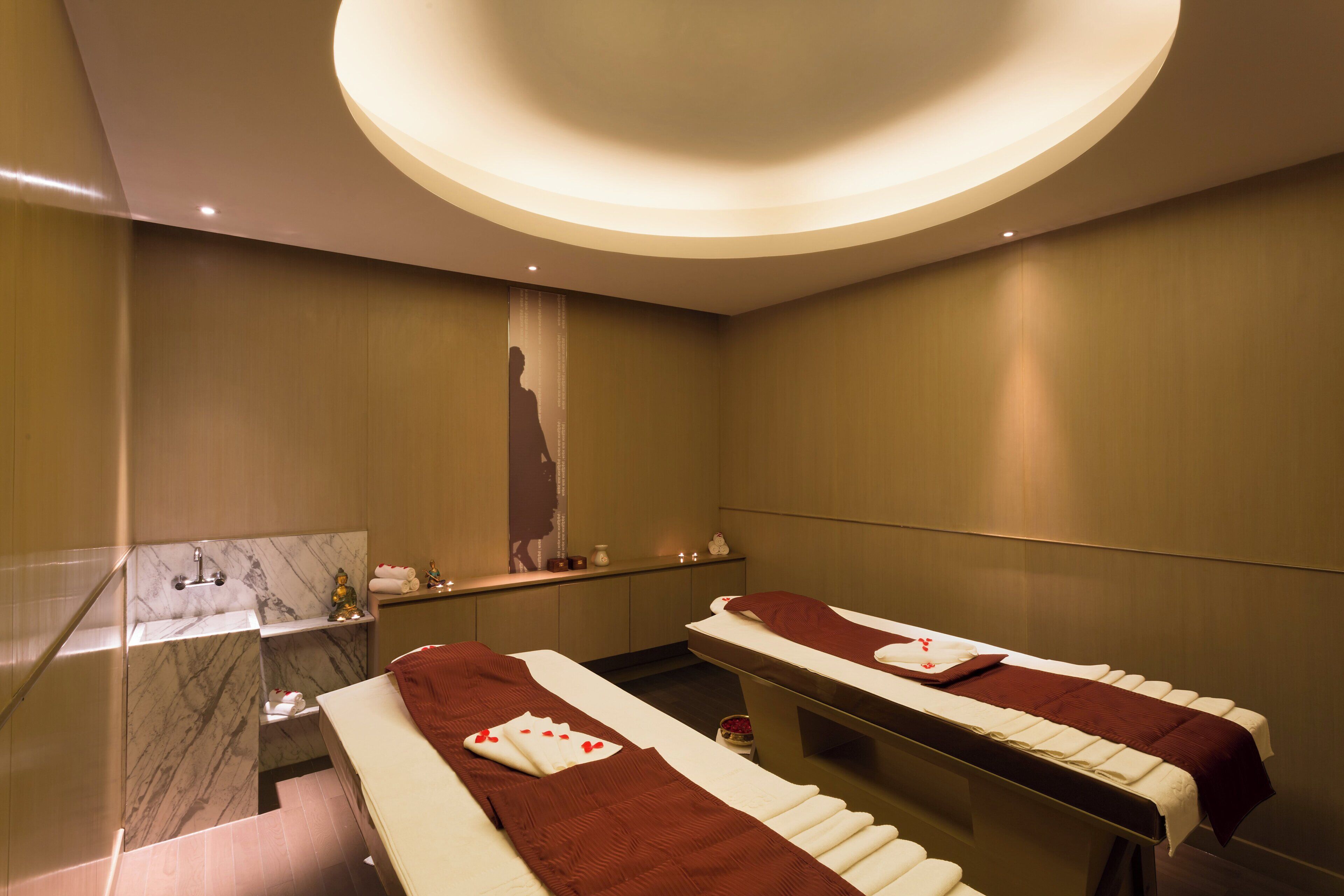 Een moderne spa-ruimte met twee massagetafels, een marmeren wastafel en een spiegel aan de muur.