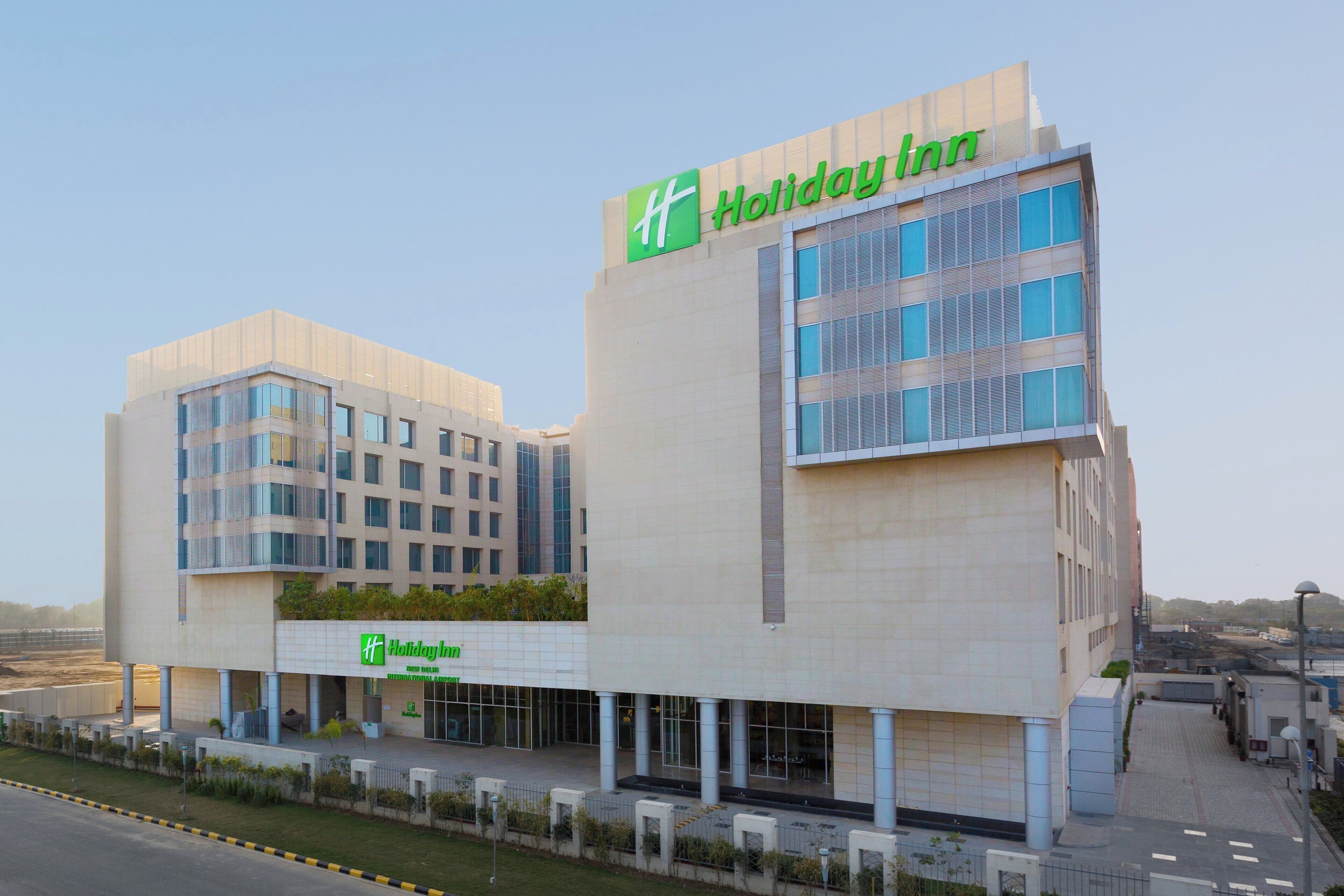 Un hotel Holiday Inn con un diseño moderno, que presenta un logo verde destacado, ventanas amplias y un techo plano.