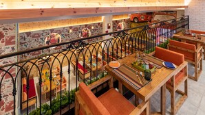 Een restaurant met houten tafels en stoelen, een muurschildering van een rode auto en een trap met een smeedijzeren leuning.