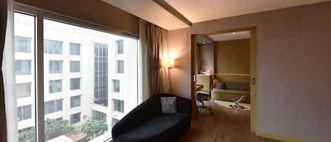 A modern hotel room with a large window, a black sofa, a desk, and a chair.