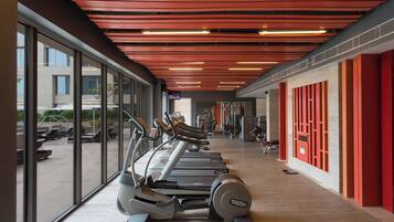 A gym with treadmills, exercise equipment, and large windows overlooking a parking area.