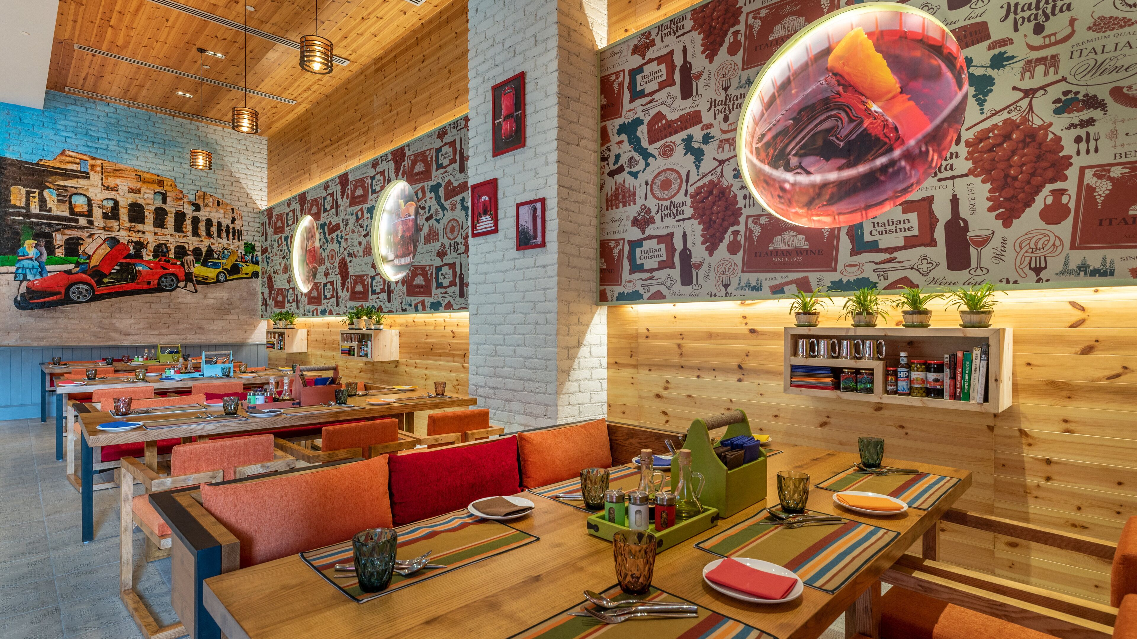 A restaurant with wooden walls, tables with orange cushions, and a mural of Italian food and wine.